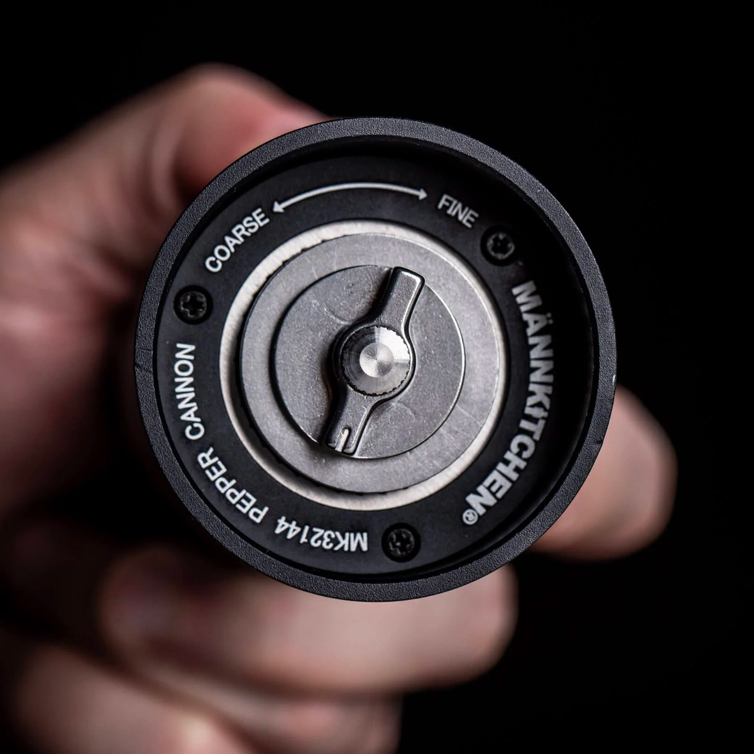 Close-up of a hand holding the Pepper Cannon, showing the grind dial marked COARSE to FINE and the MÄNNKITCHEN MK32144 stamp on the base.