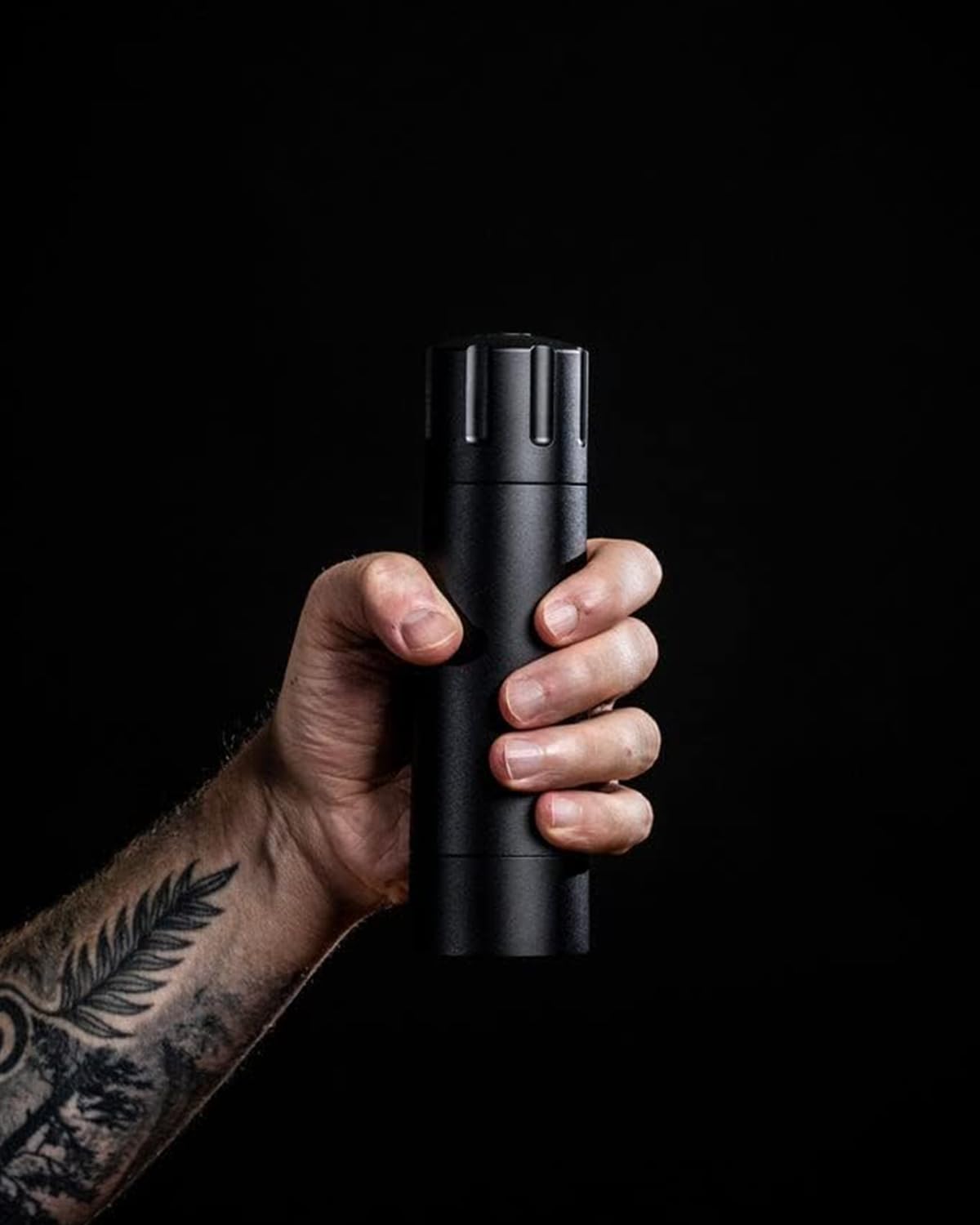 A hand gripping the black Pepper Cannon against a dark background.
